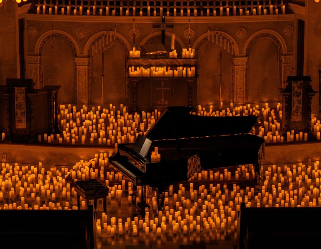 A piano is displayed on a stage surrounded by hundreds of candles.