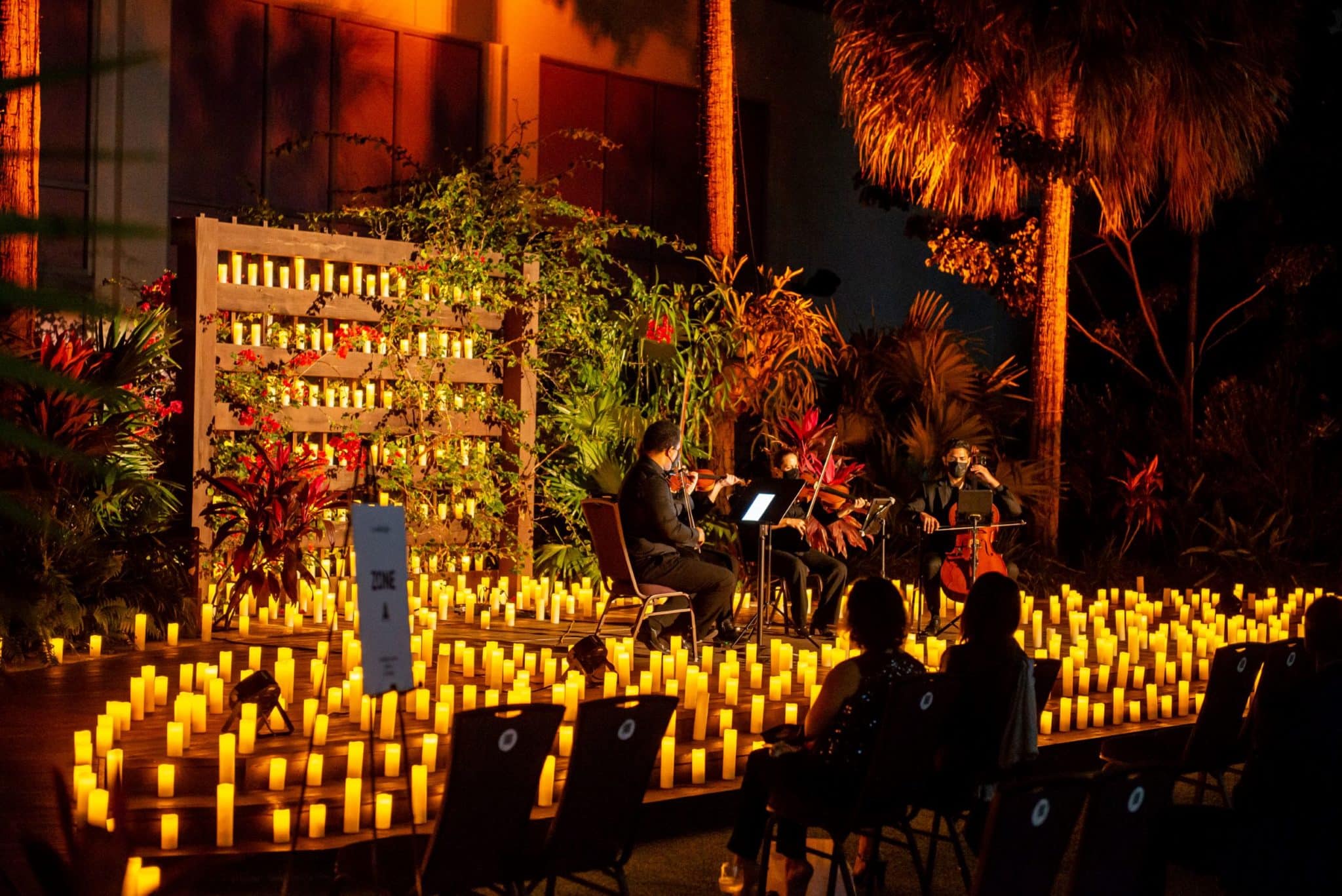 A string quartet is performing outdoors at Jungle Island on a stage covered in candles with the silhouette of a couple watching in the audience.