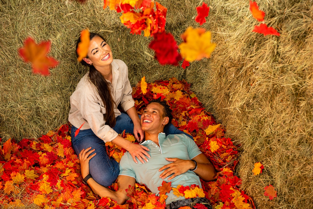Two people laying in a leaf pit surrounded by hay