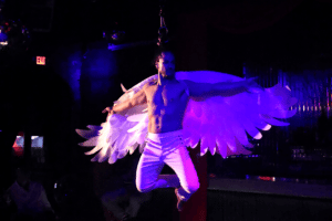 A shirtless man flies through the air wearing angel wings