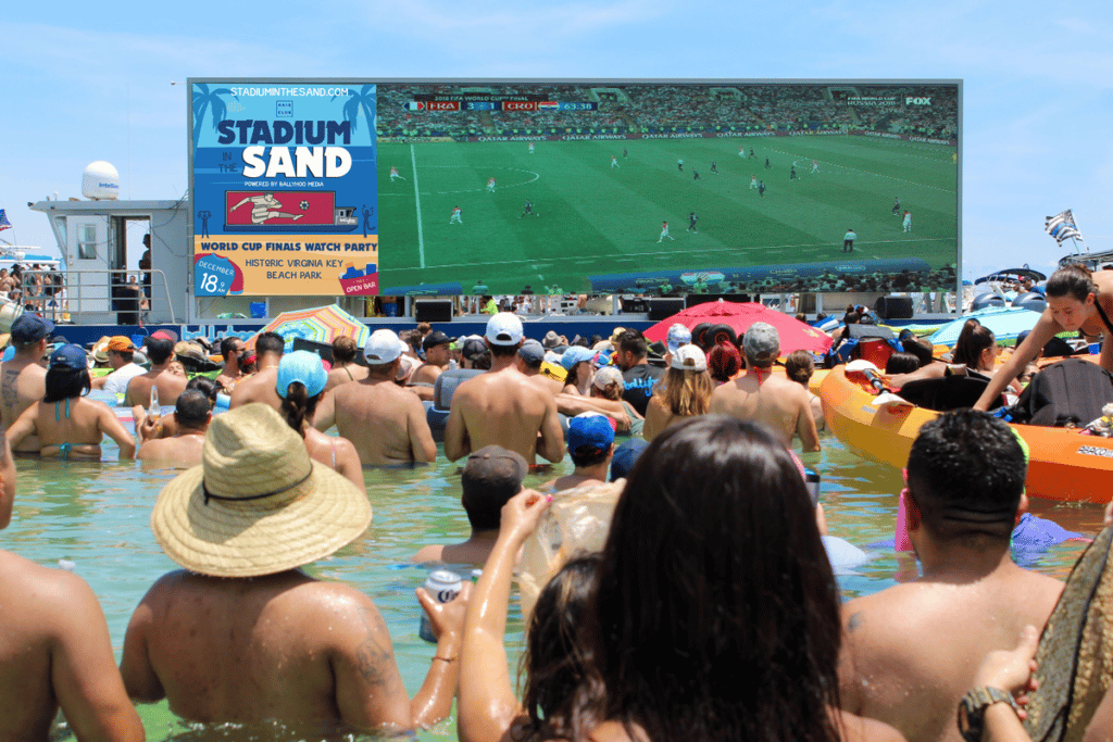 A watch party being held in the water as people look onto a floating screen playing sports