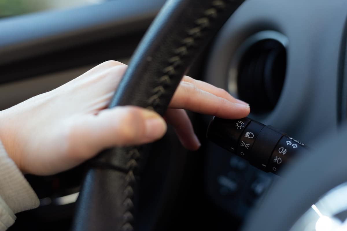Woman turning on left signal switch, close up shot of her hand. Car interior details.