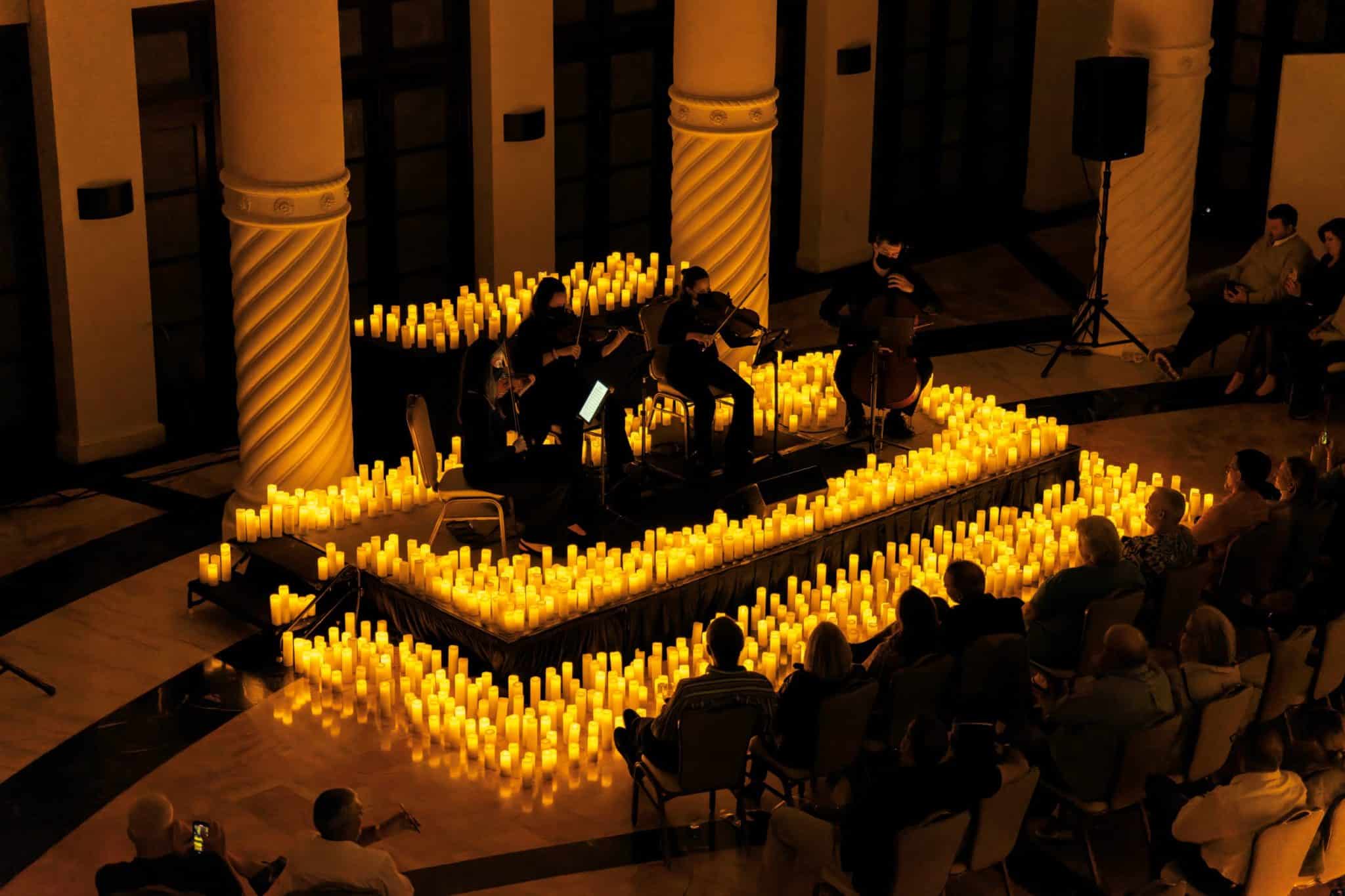 A string quartet performing on a stage covered in candles inside Coral Gables Congregational Church.