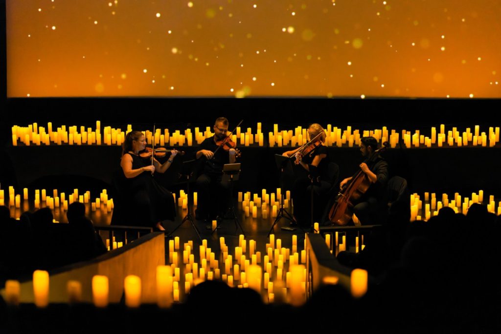 a string quartet performing on stage, surrounded by countless candles