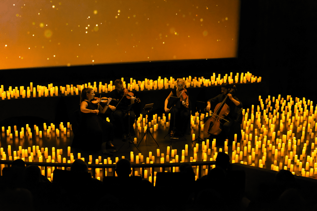A string quartet performing on a stage covered in candles with a screen of lights in the background.