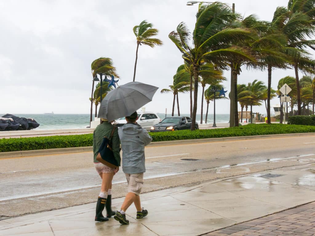 People walking with umbrella in heavy rainfall during tropical storm on seaside boulevard in Fort Lauderdale, Florida, USA