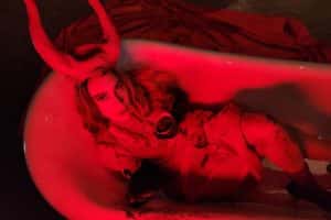 A woman wearing devil's horns lays in a bathtub